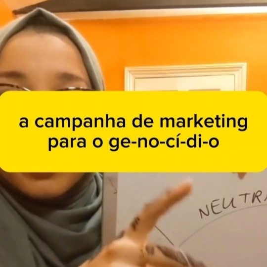 'a campanha de marketing para o genocídio' em preto sobre fundo amarelo em cima de um frame de vídeo mostrando uma mulher de pele marrom clara usando óculos e hijab cinza e segurando uma lousa branca